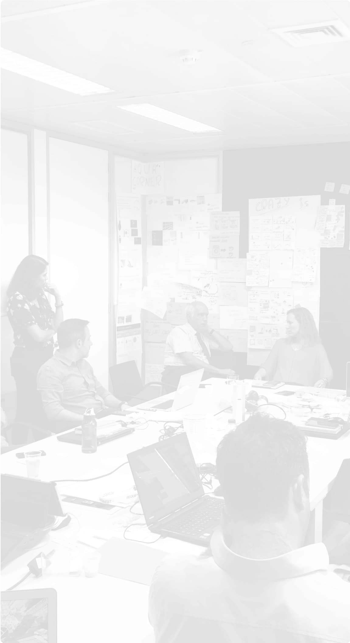 Brainstorming session in a meeting room with notes on the walls. Group of people in a meeting room participating in a brainstorming session. The room is filled with post-it notes and annotations on the walls, and several people are seated around a table with laptops and papers.