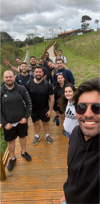 A group of people posing for a photo on a wooden trail outdoors. The group is smiling and seems to be enjoying a hike on a cloudy day.