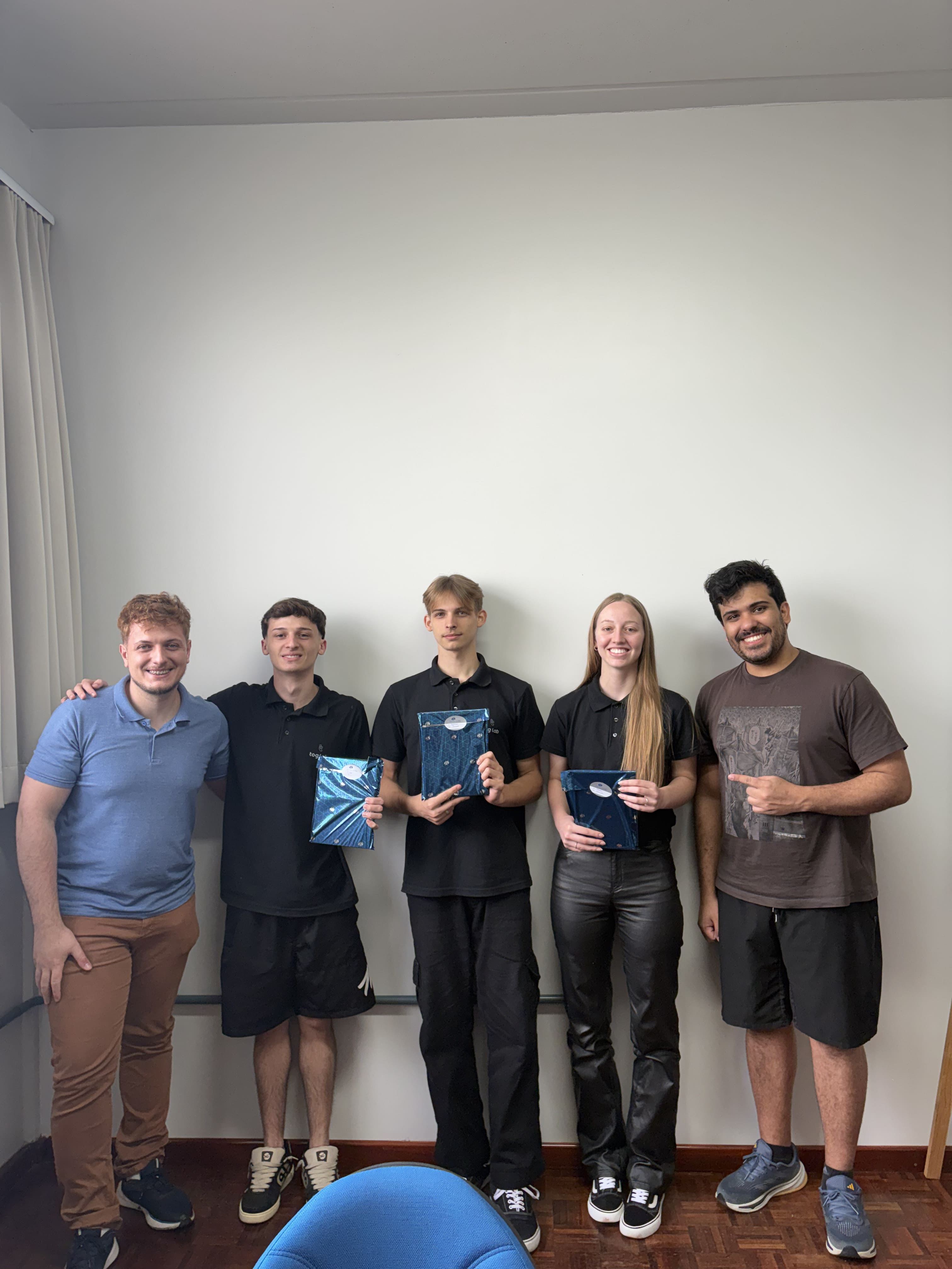Team members holding branded notebooks after presentation. Five team members standing side by side indoors, some holding blue branded notebooks and smiling at the camera.