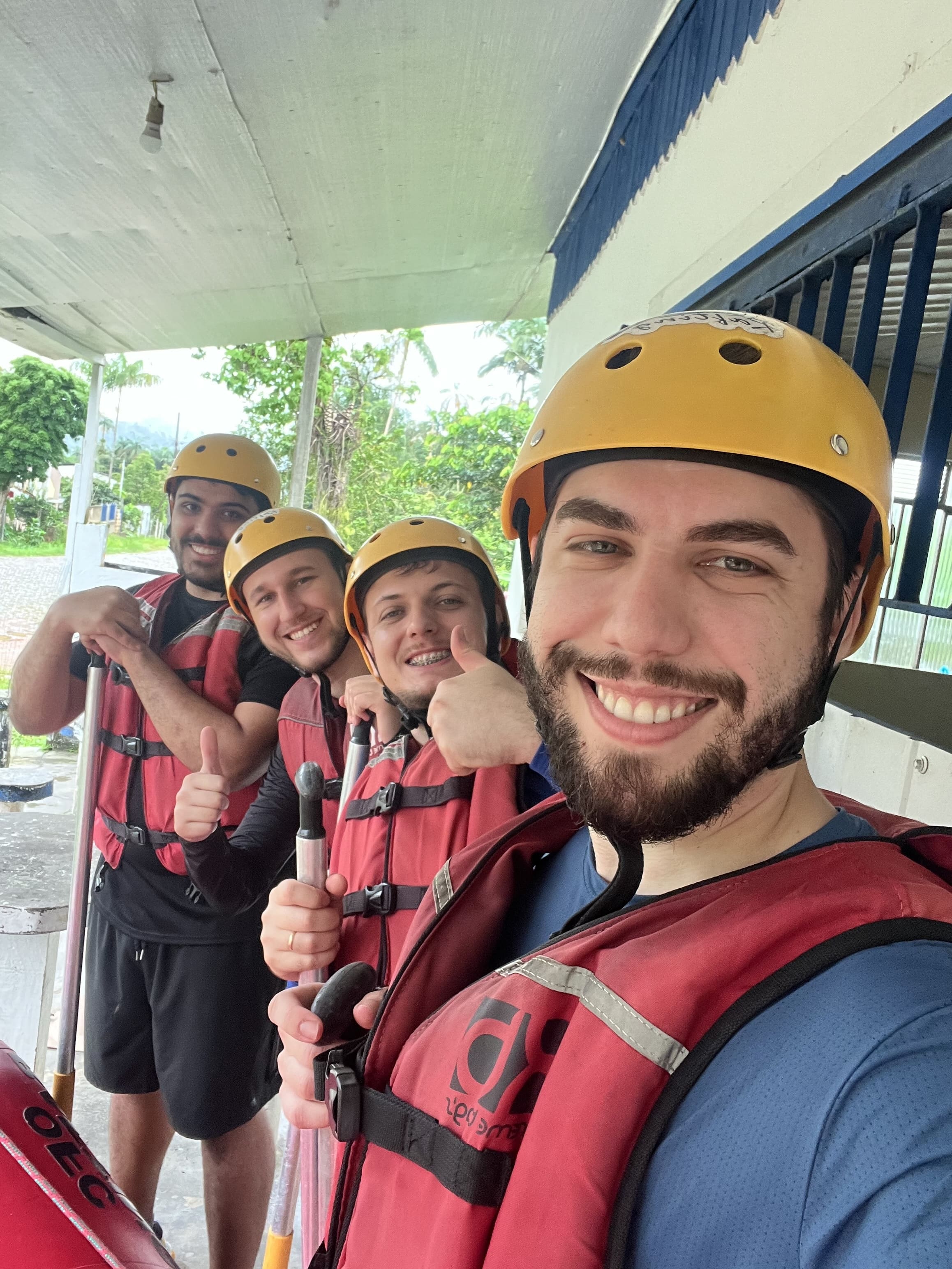 Team members ready for a whitewater rafting adventure. Four team members wearing helmets and life jackets smiling and giving thumbs up while holding paddles before a rafting activity.