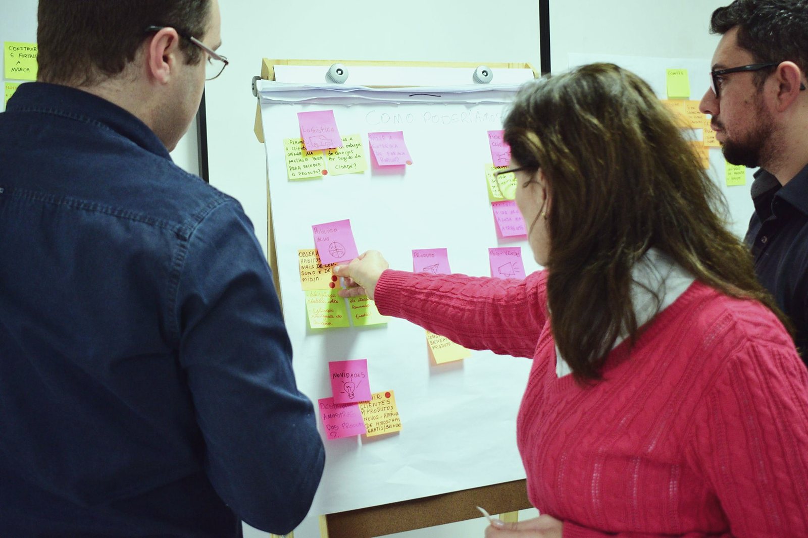 Three people in front of a board of sticky notes, choosing an idea